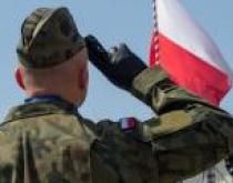 Żołnierz salutujący przed flagą Polski